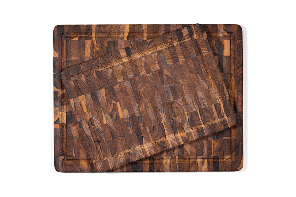 Stacked rectangular end grain teak cutting boards with juice canals and natural wood patterns.
