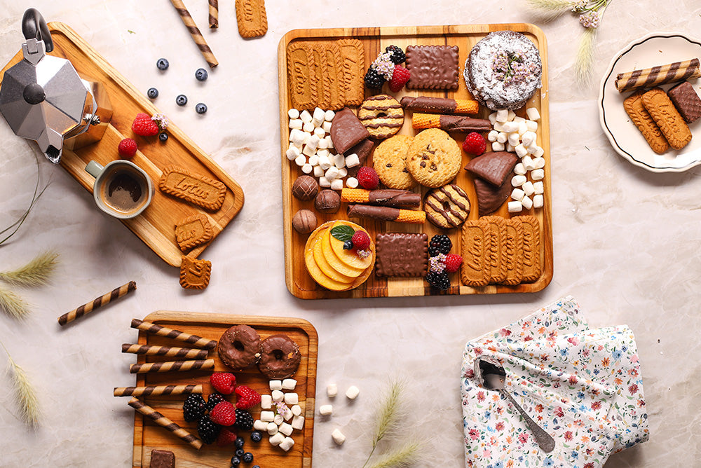 Square teakwood serving trays featuring an assortment of desserts, cookies, and berries on a marble surface.