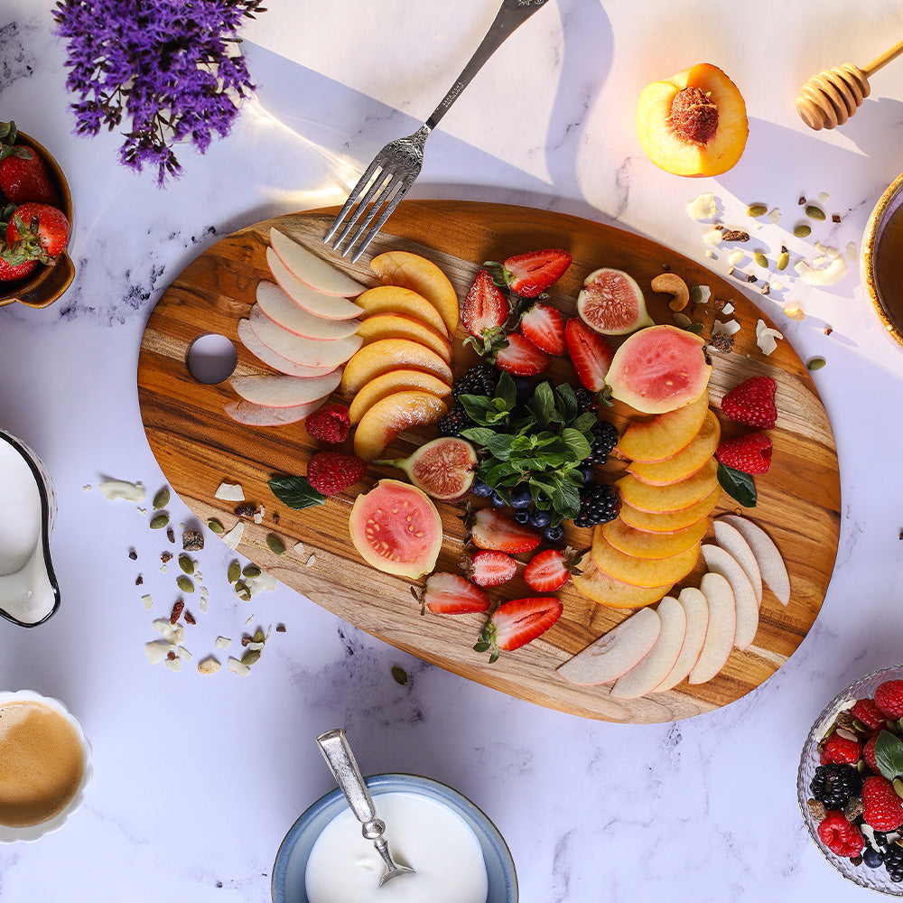 Elegant oval teakwood serving board featuring an arrangement of fresh sliced fruits on a marble surface.
